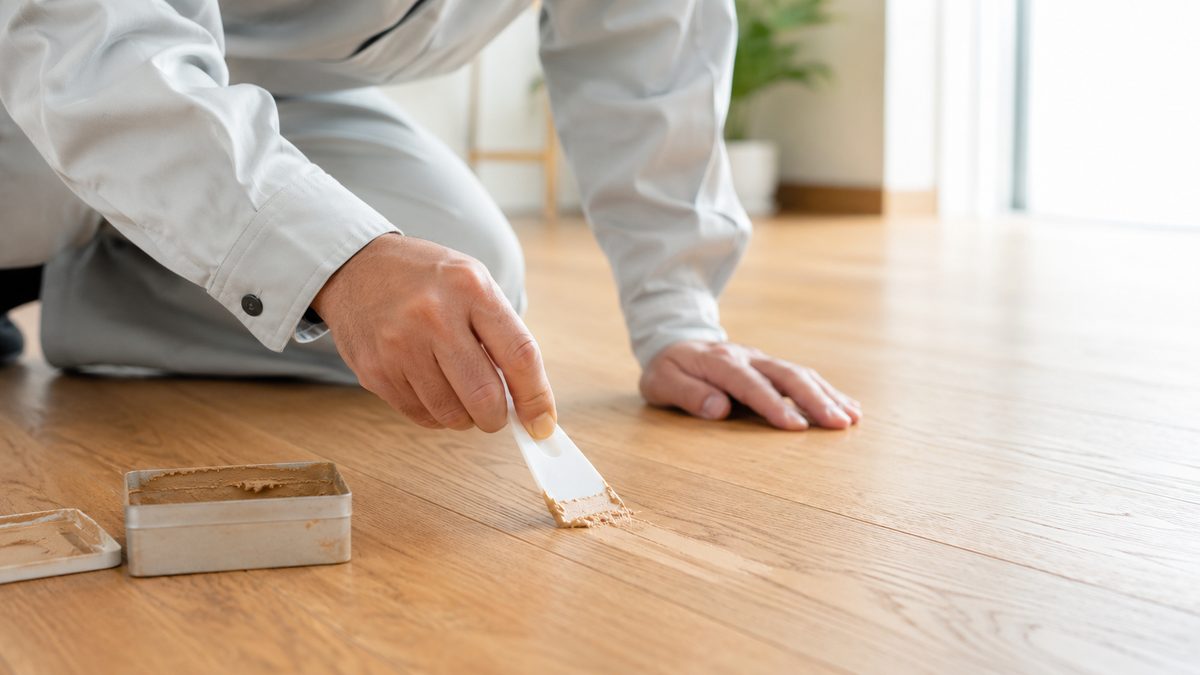 フローリングの傷を補修する作業着の職人の手元